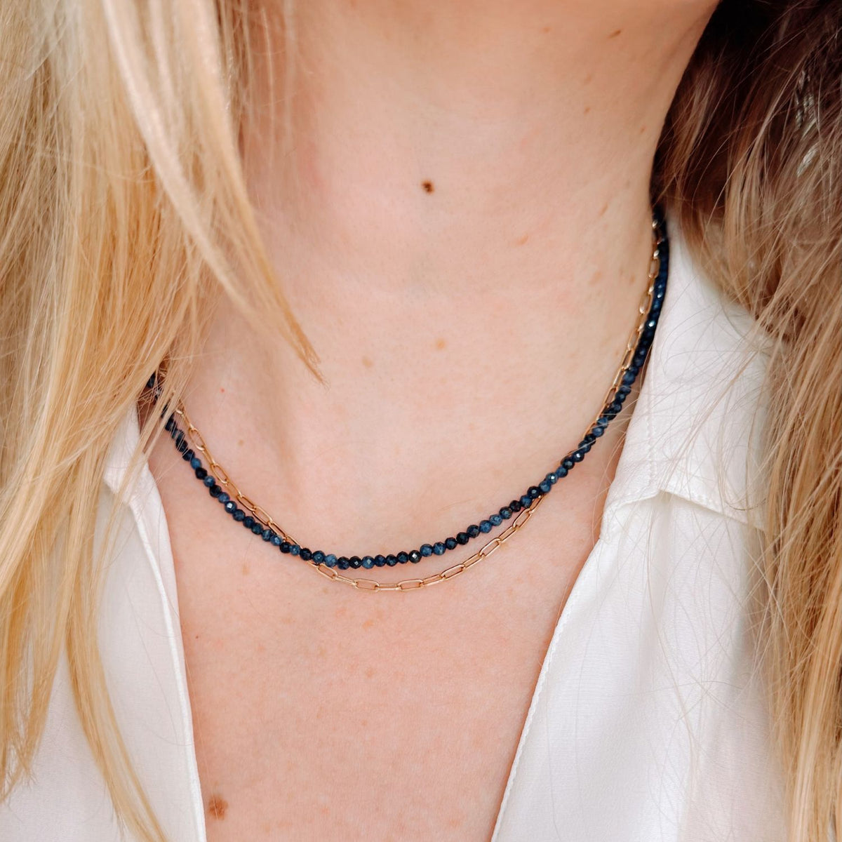 Close-up of a person wearing a delicate necklace with blue sapphire beads and gold chain.
