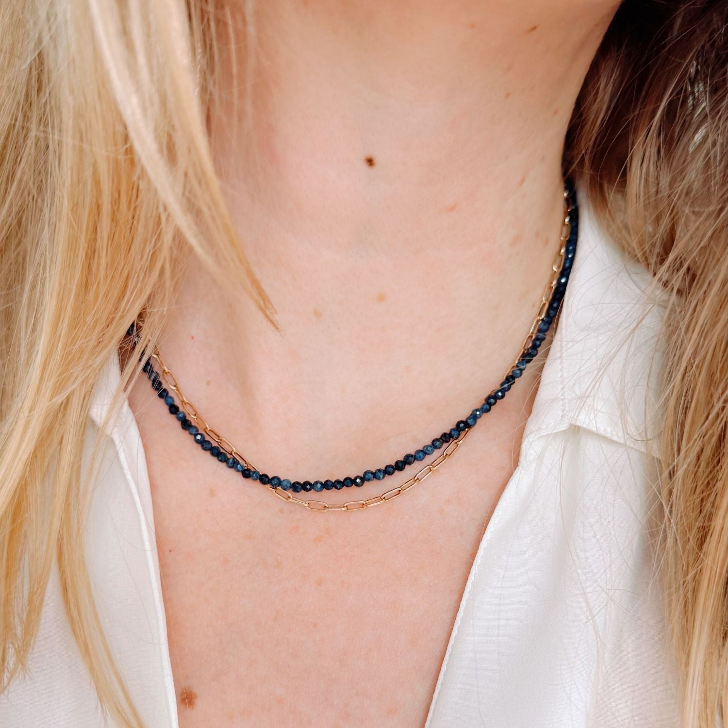 Close-up of a person wearing a delicate necklace with blue sapphire beads and gold chain.