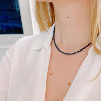 Person wearing a blue sapphire beaded necklace with a blurred background