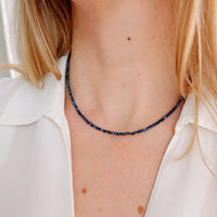 Person wearing a blue sapphire beaded necklace with a white shirt
