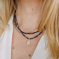 Close-up of a person wearing multiple blue sapphire necklaces with a focus on a gold star moon tarot pendant.