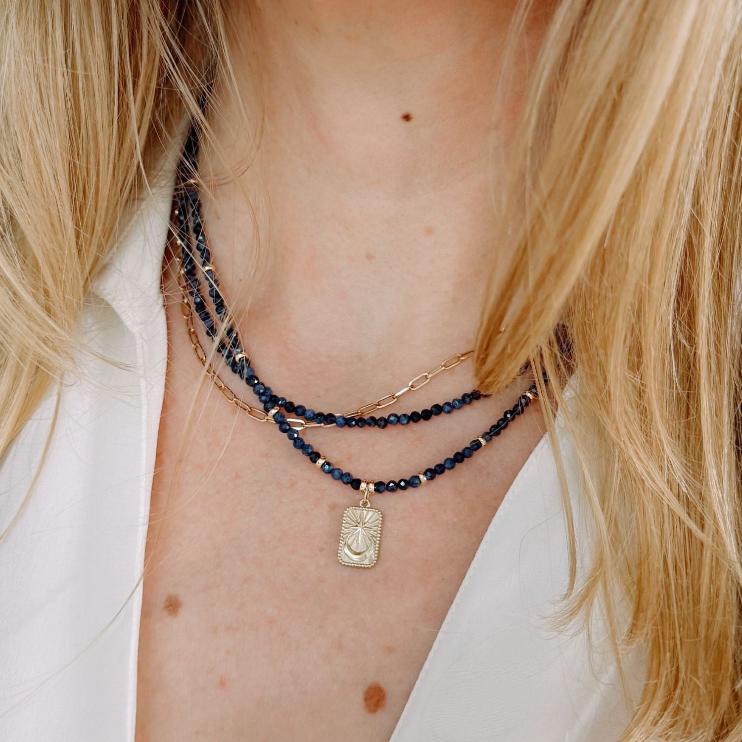 Close-up of a person wearing multiple blue sapphire necklaces with a focus on a gold star moon tarot pendant.
