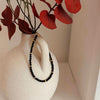Black Spinel beaded bracelet with 14k gold accents on a textured white vase with red leaves.