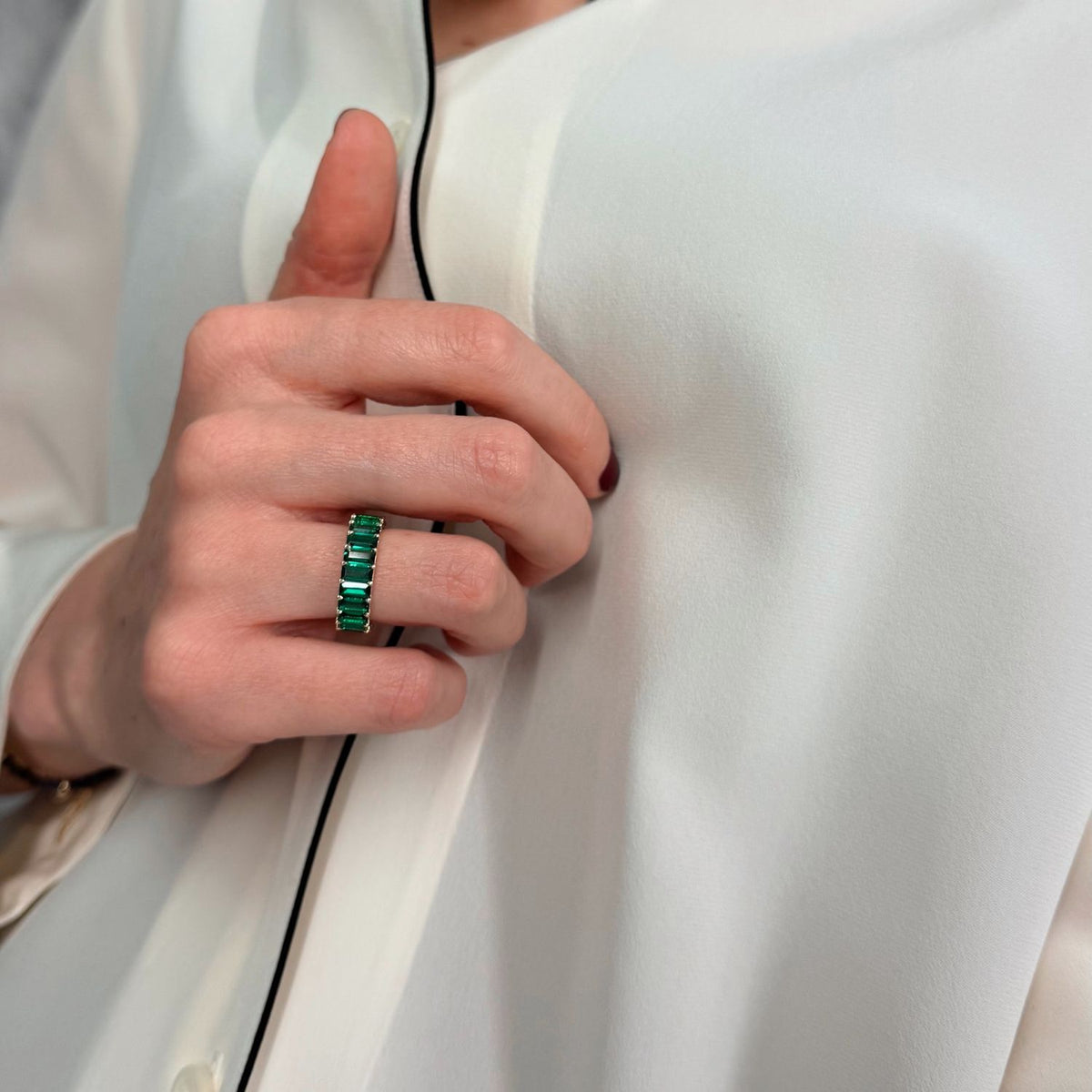 woman's hand wearing an emerald eternity ring against white shirt
