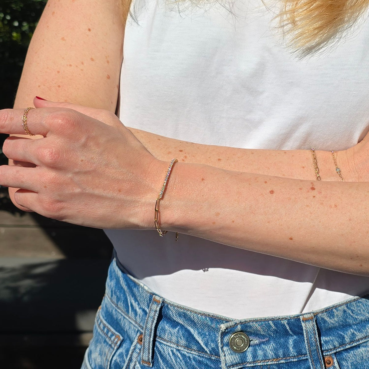 woman crossing her arms and on her wrist is a gold chain and diamond bracelet