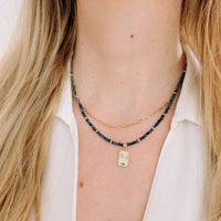 Necklace with blue sapphire beads and a star moon gold tag worn by a person with blonde hair.