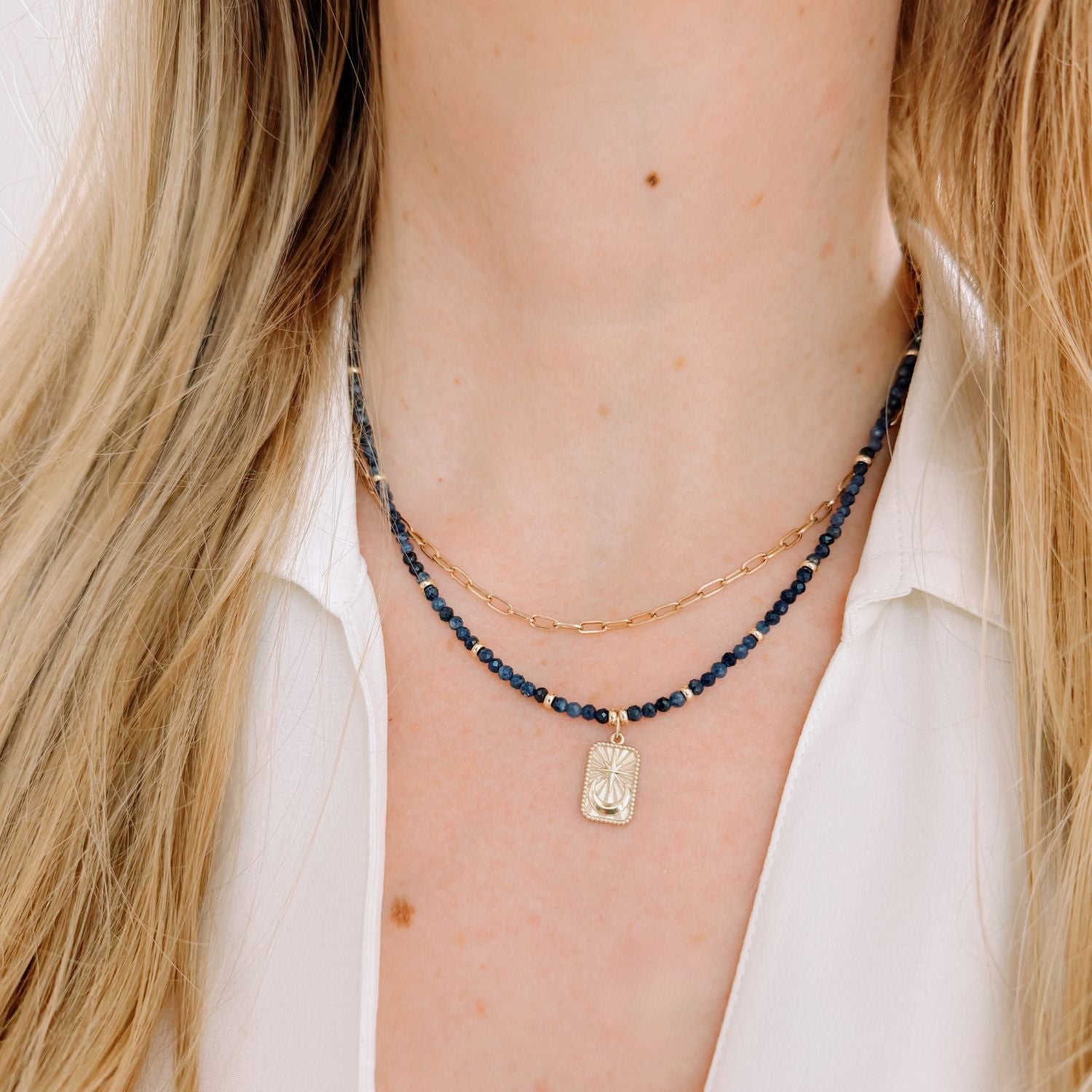Necklace with blue sapphire beads and a star moon gold tag worn by a person with blonde hair.