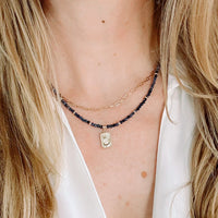 Necklace with blue sapphire beads and a gold pendant on a person wearing a white shirt.