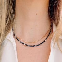 Close-up of a person wearing two necklaces: one gold and one blue sapphire.