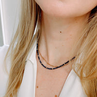 Close-up of a person wearing a delicate necklace with blue beads and gold chain.