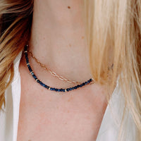 Close-up of a person wearing a gold and blue beaded necklace.