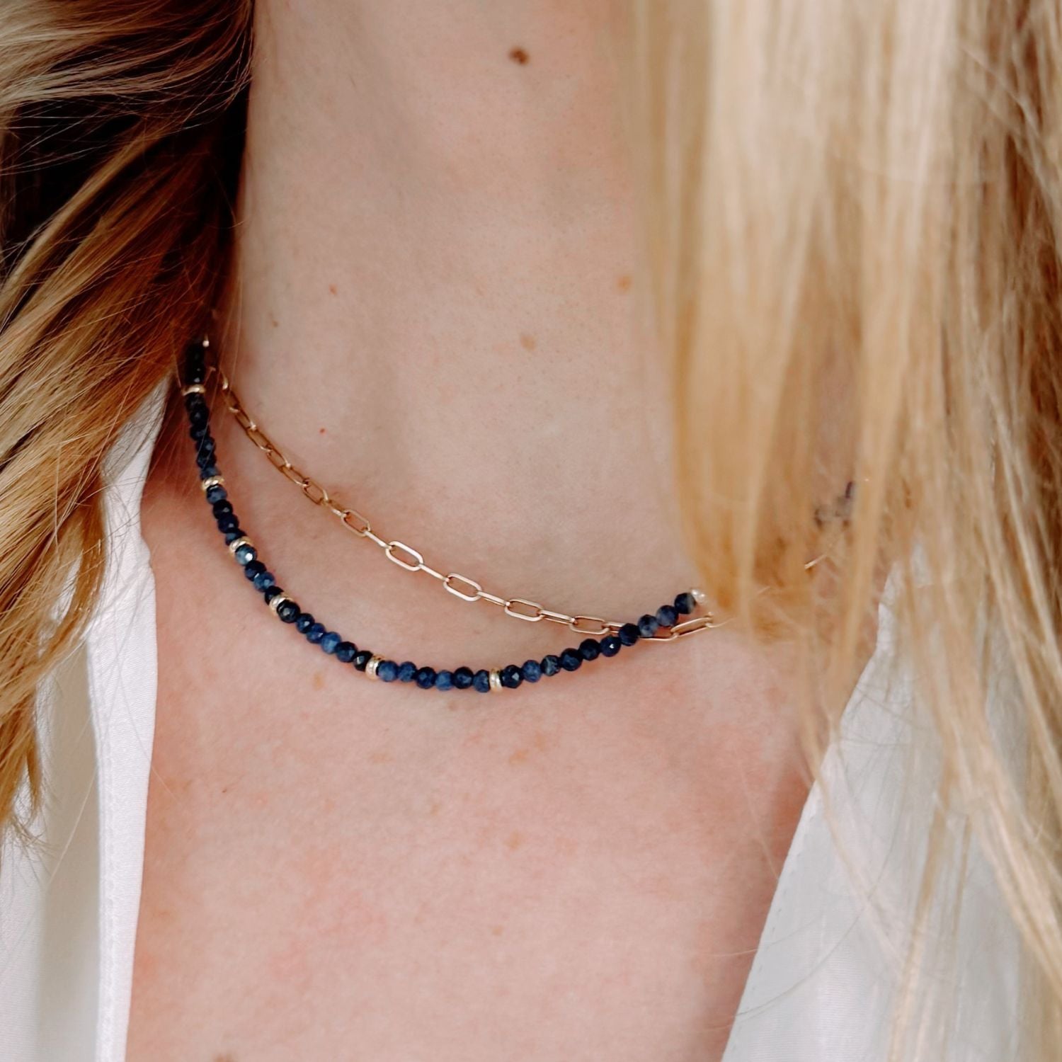 Close-up of a person wearing a gold and blue beaded necklace.