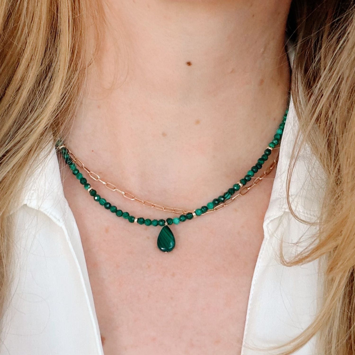 Close-up of a person wearing a green beaded necklace with a teardrop pendant.