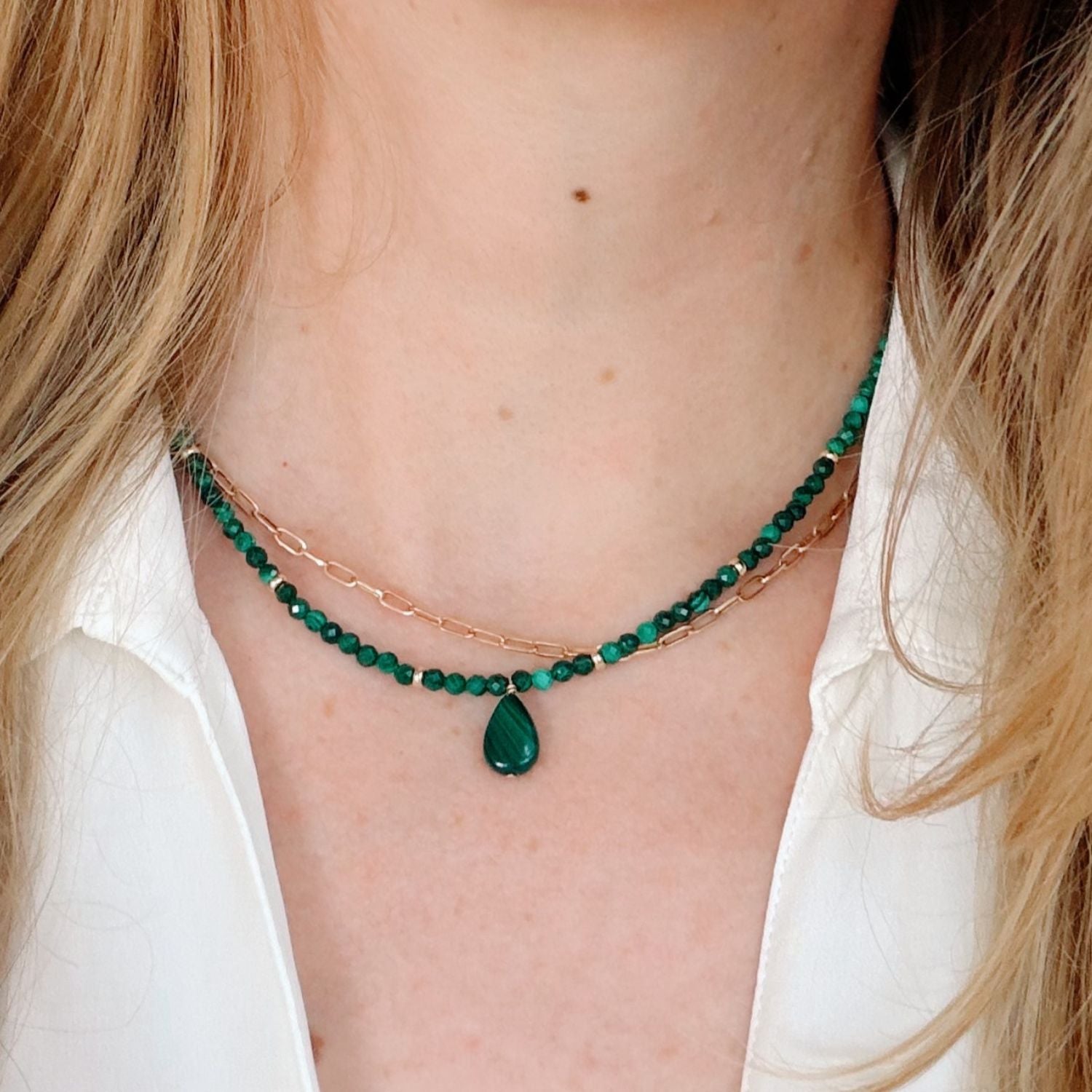 Close-up of a person wearing a green beaded necklace with a teardrop pendant.