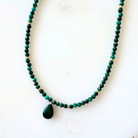 Green beaded necklace with a large green pendant on a white background