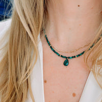 Close-up of a person wearing a green beaded necklace with a teardrop pendant.