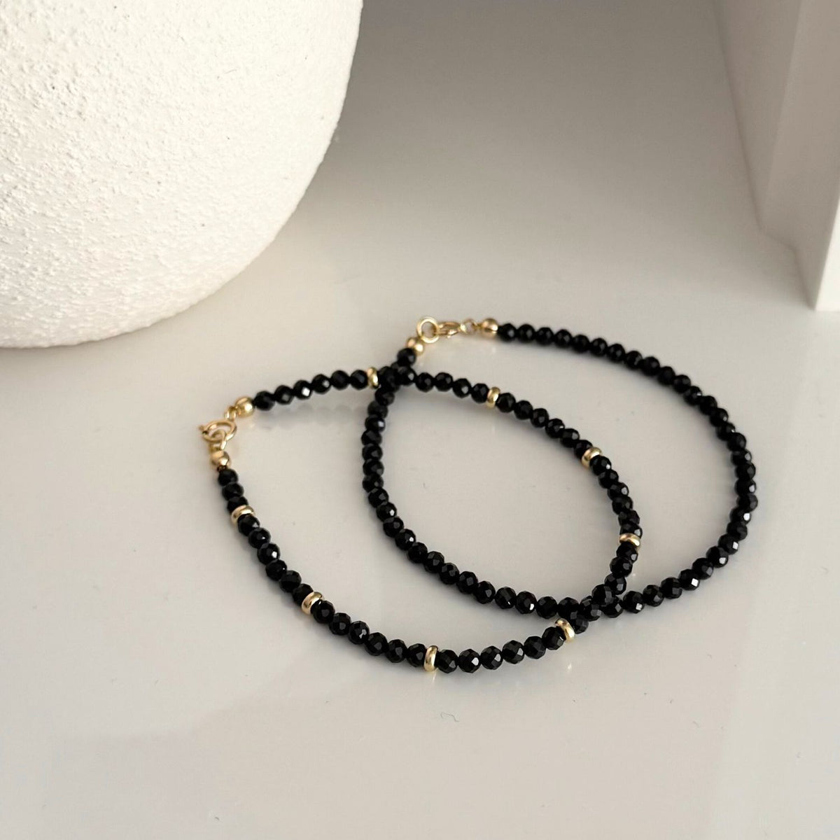 Black Spinel beaded bracelet set with gold accents on a light gray surface