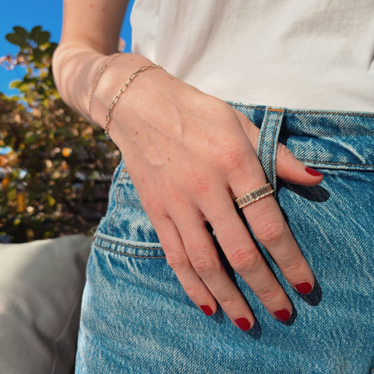 woman wearing a baguette eternity diamond ring with her hand in her jeans and red nail polish