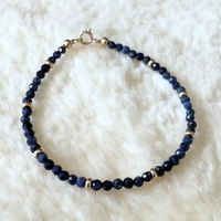 Navy blue sapphire beaded bracelet with gold accents on a white fluffy surface