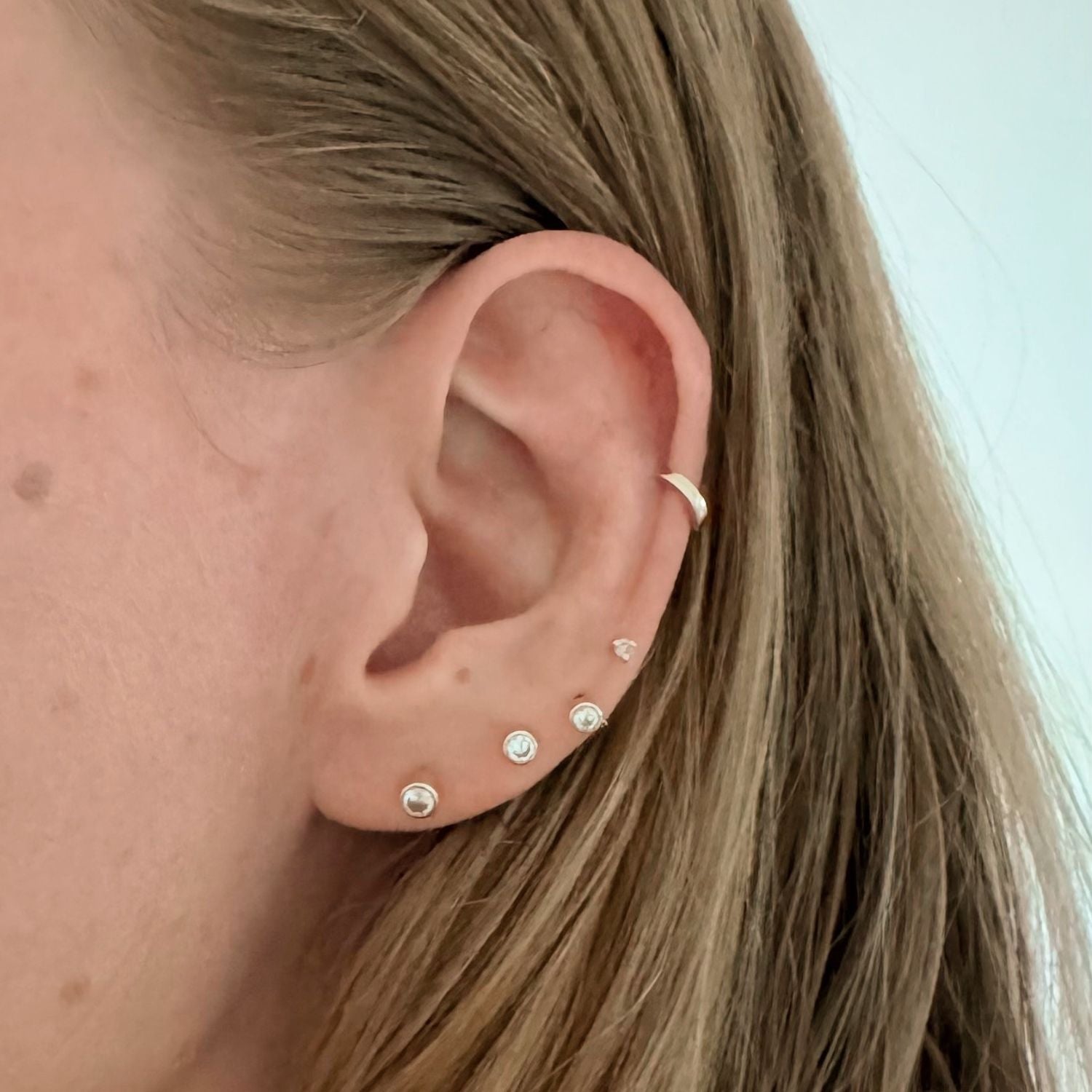 Close up of ear modeling 14k gold diamond studs and a gold huggie cartilage earring. 