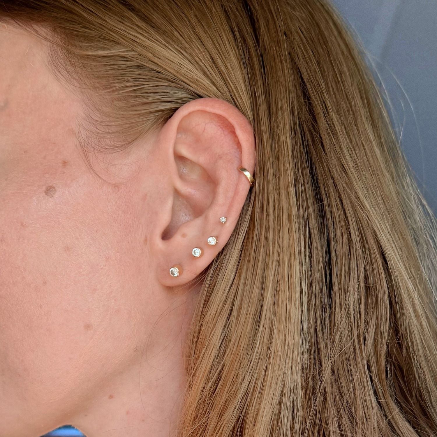 Close up of ear modeling 14k gold diamond studs and a gold huggie cartilage earring. 