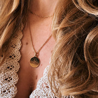 Close-up of a person wearing a gold necklace with a circular pendant, surrounded by beige lace fabric.
