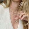 Close-up of a person wearing a gold necklace with a north star pendant, set against a neutral background.