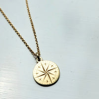 Gold necklace with a compass pendant on a light gray background