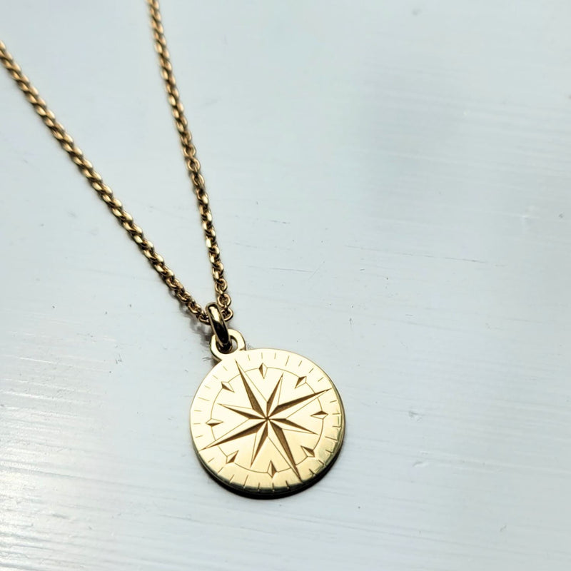Gold necklace with a compass pendant on a light gray background