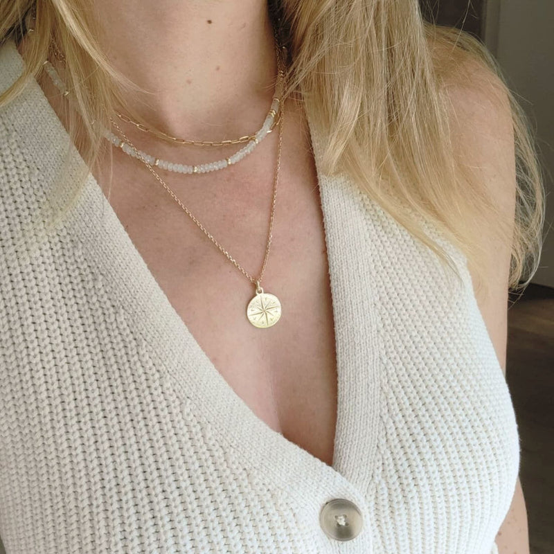Close-up of a person wearing a gold necklace with a star pendant, against a neutral background.