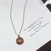 Rose gold necklace with a compass pendant on a white paper background with text.