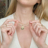 Person wearing a gold necklace with a compass pendant, holding it with both hands.