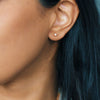 Close-up of an ear with a small gold cube stud earring against a blurred background