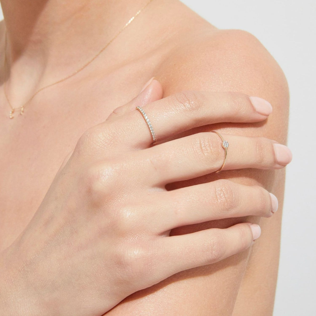Close-up of a hand wearing two diamond rings on a light background