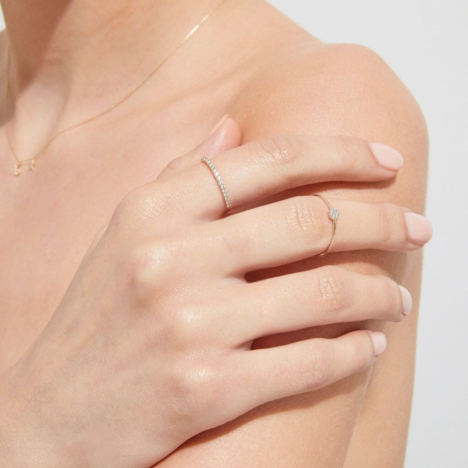 Close-up of a hand wearing two diamond rings on a light background