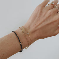 14k gold fairmined paperclip chain bracelet with lab diamond bezel worn on wrist with gold chain and blue sapphire bracelets 