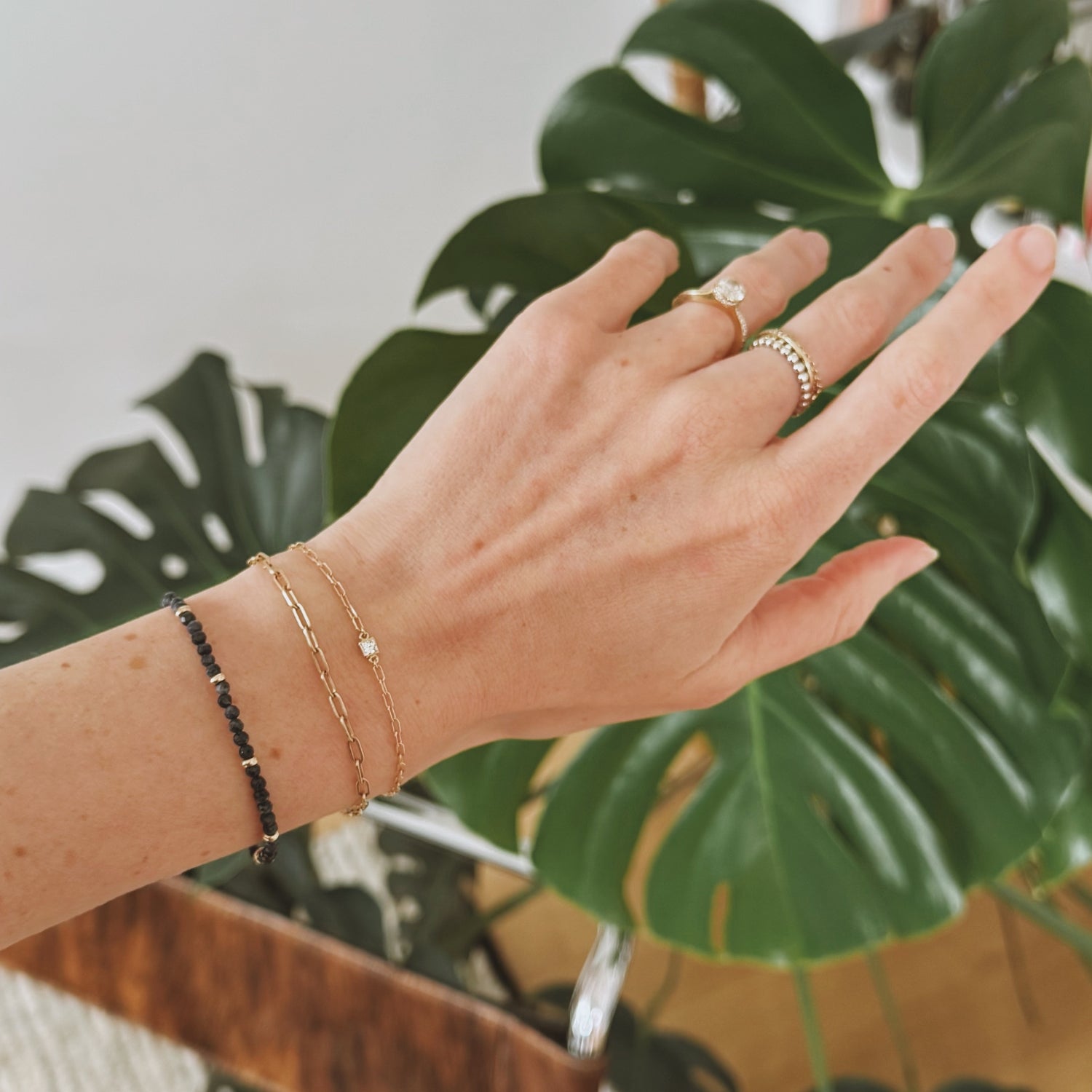 14k gold fairmined paperclip chain bracelet with lab diamond bezel modeled with two other 14k gold bracelets and plant in background