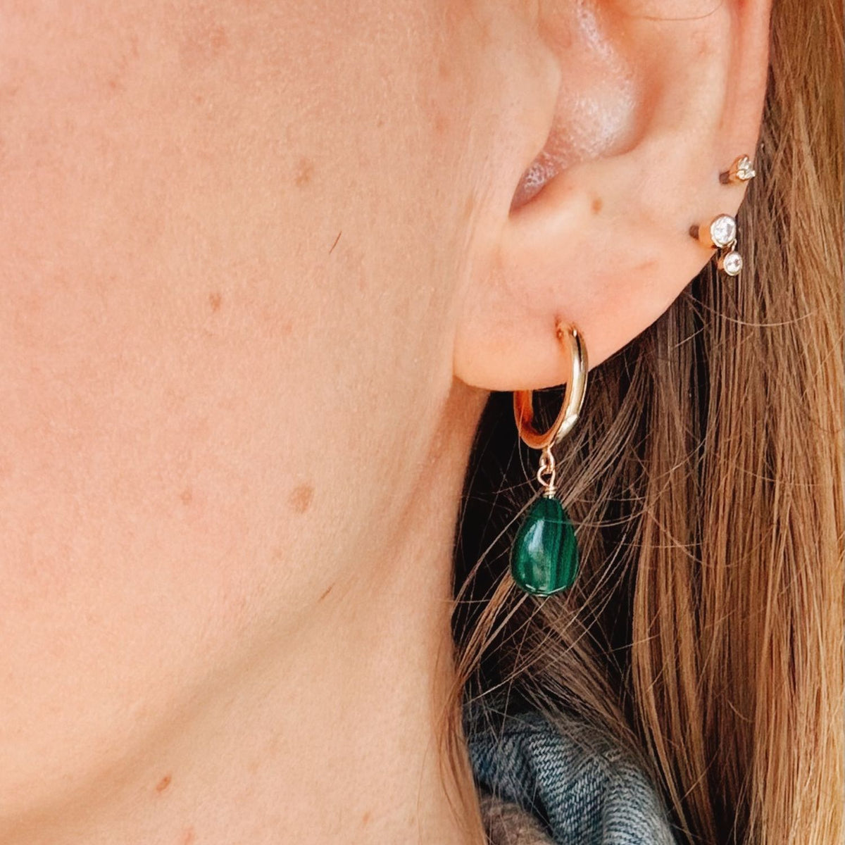 Close-up of an ear wearing gold hoop earrings with green teardrop charms.