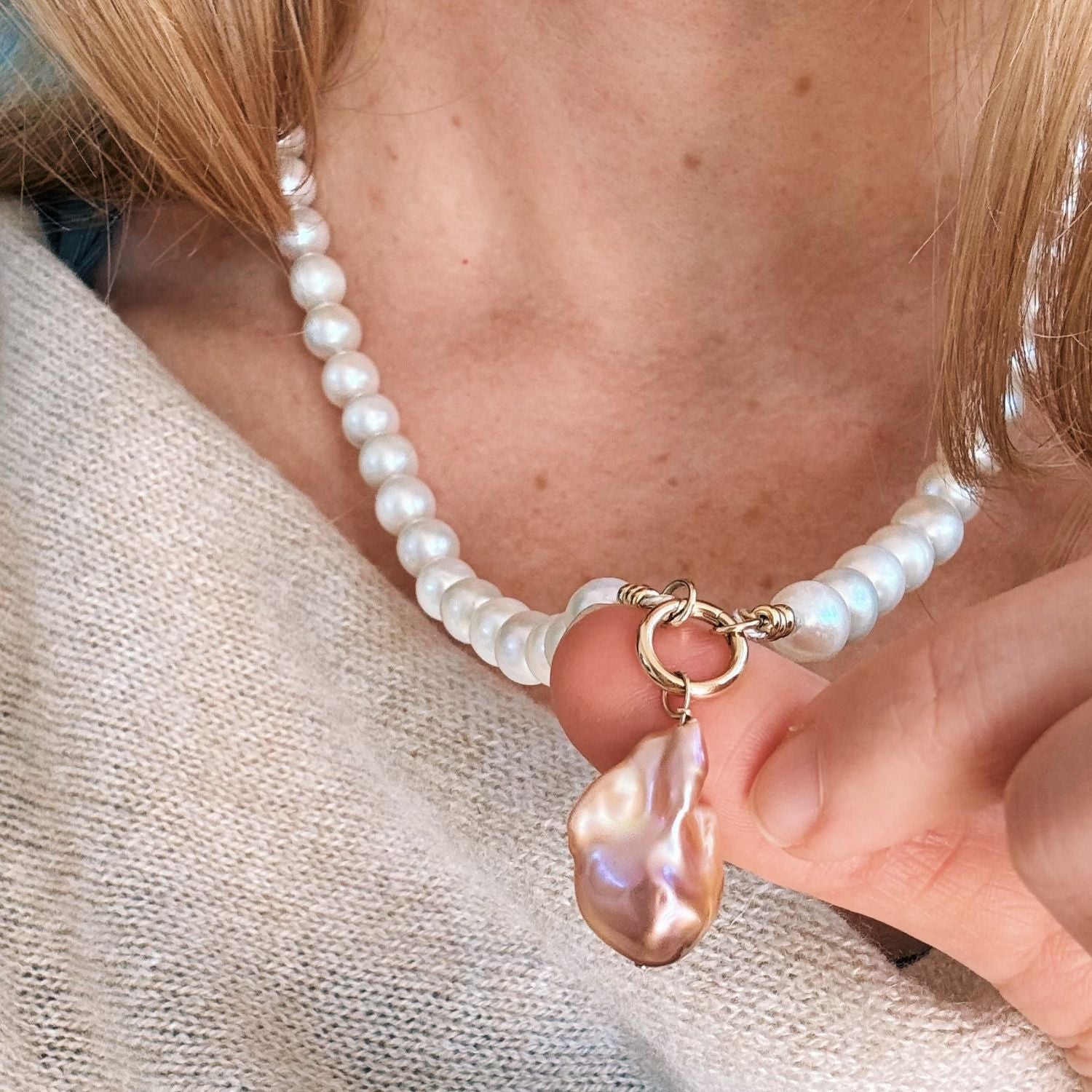 Pearl necklace with a large baroque pearl pendant held by a person wearing a light-colored sweater.