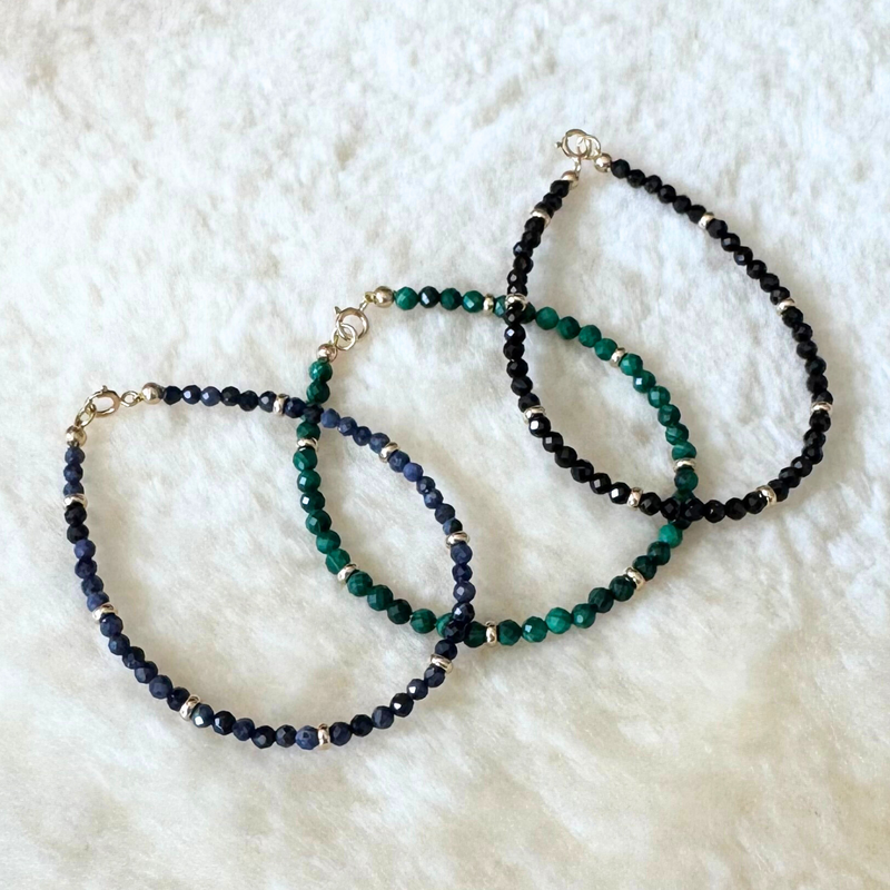 Three beaded bracelets in blue, green, and black on a white textured surface