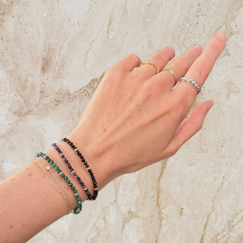 Hand wearing multiple rings and bracelets on a marble surface
