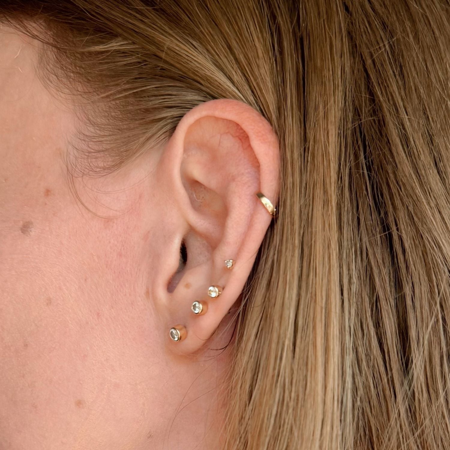 Close up of ear modeling 14k gold diamond studs and a gold huggie cartilage earring. 