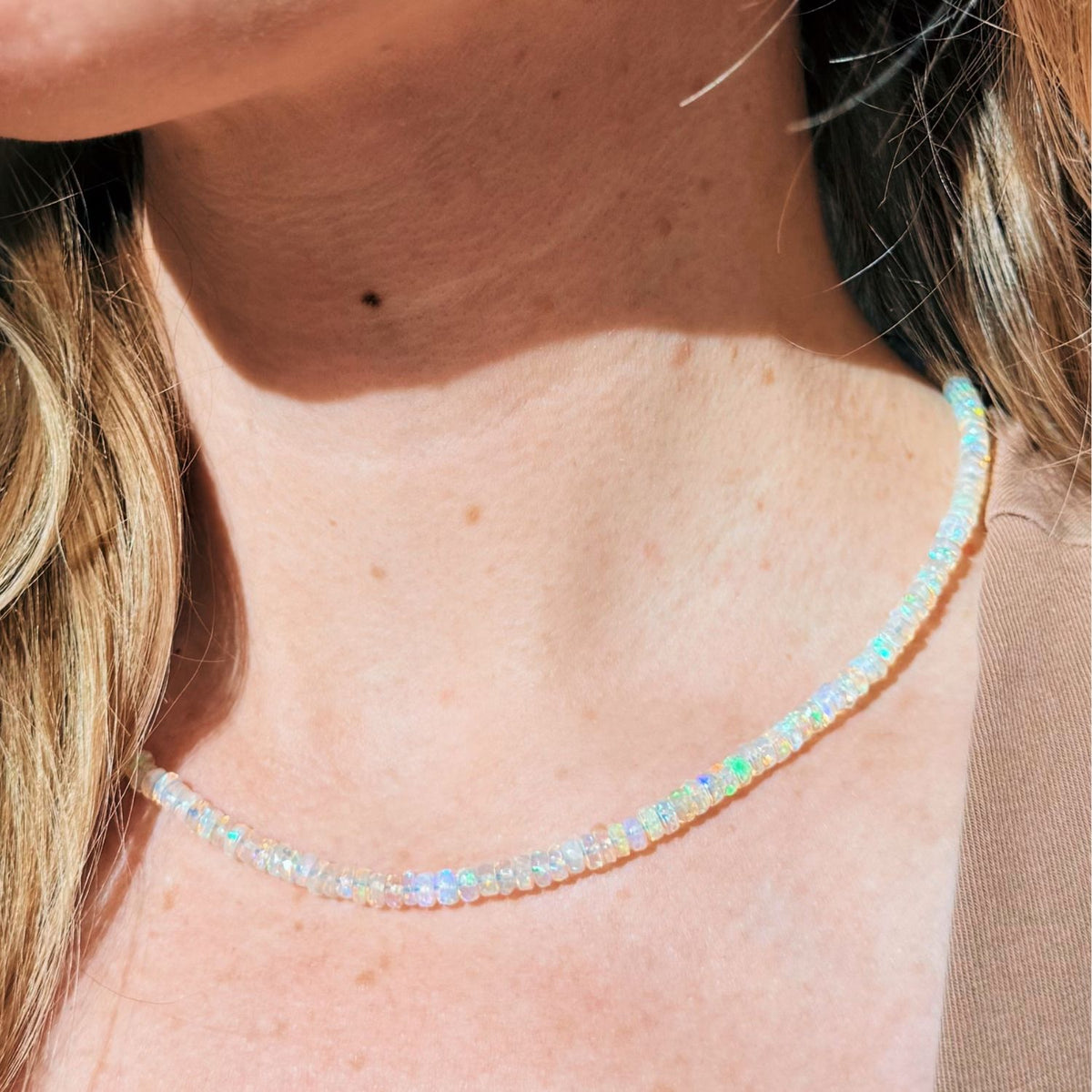 A close-up of a person's neck wearing a delicate opal beaded necklace with iridescent, opalescent beads that shift colors under sunlight.