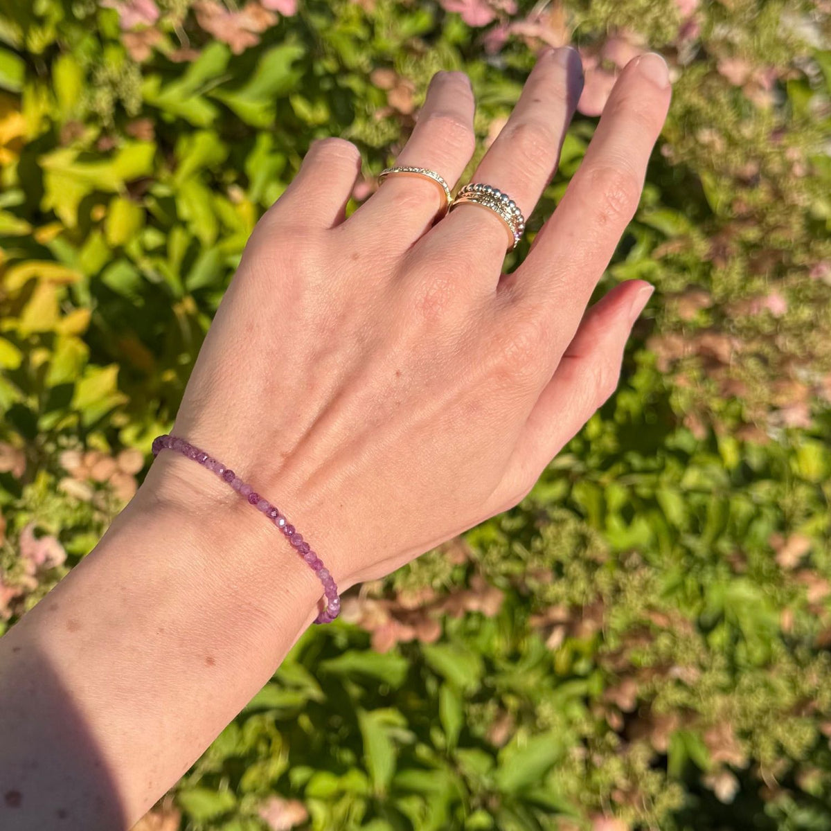 woman wearing a pink ruby bead bracelet with leaves in the background