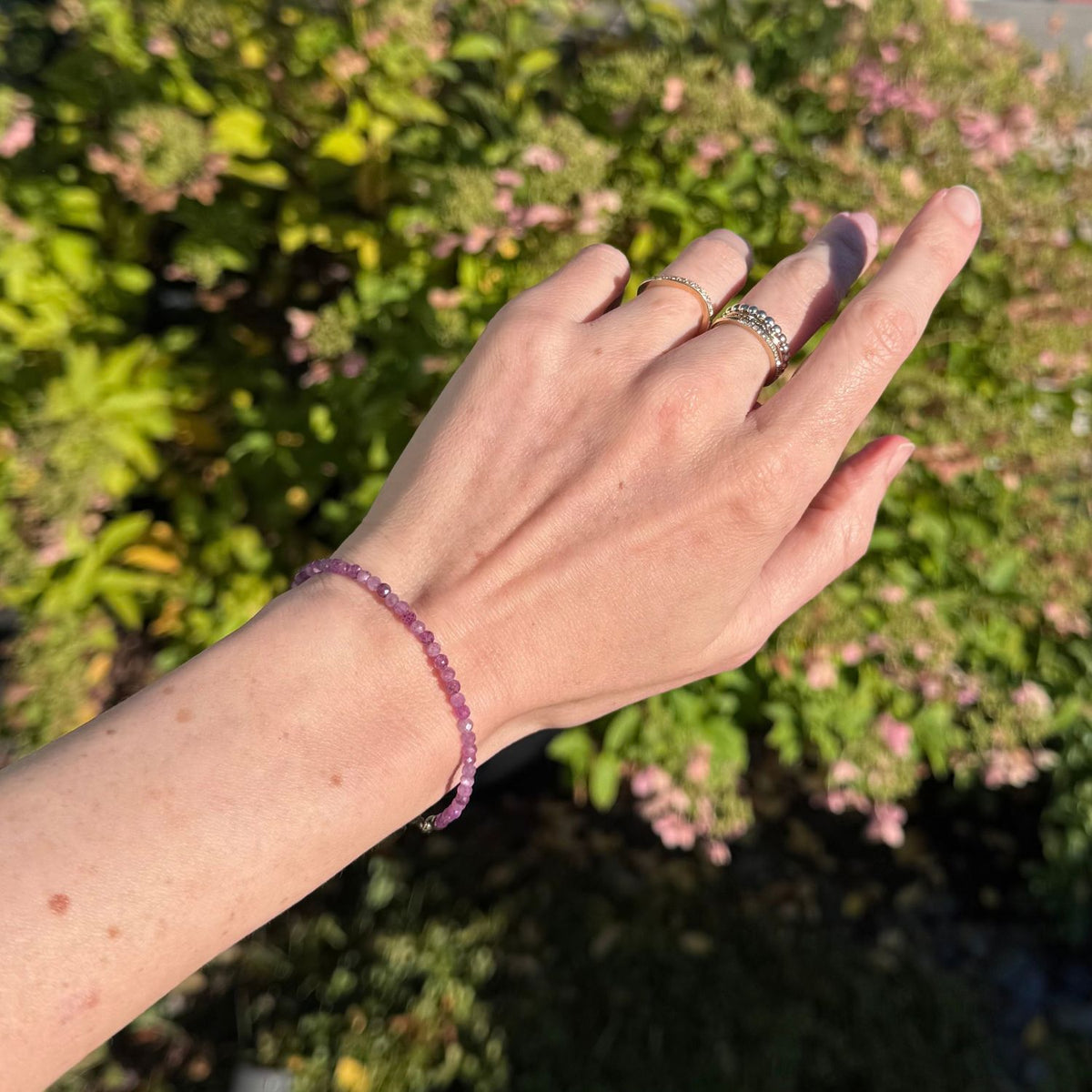 woman's wrist wearing a pink ruby bead bracelet with leaves and flowers in the background