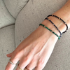 Close-up of a wrist wearing three 14k gold gem beaded bracelets on a neutral background