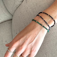 Close-up of a wrist wearing three 14k gold gem beaded bracelets on a neutral background