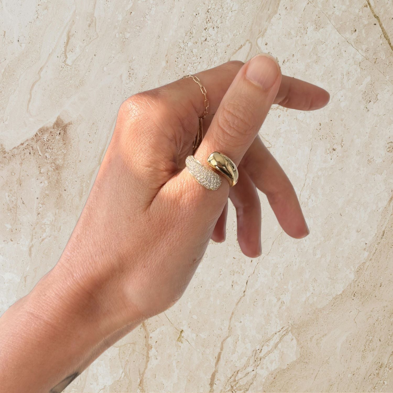 Hand wearing two yellow gold rings on a marble background