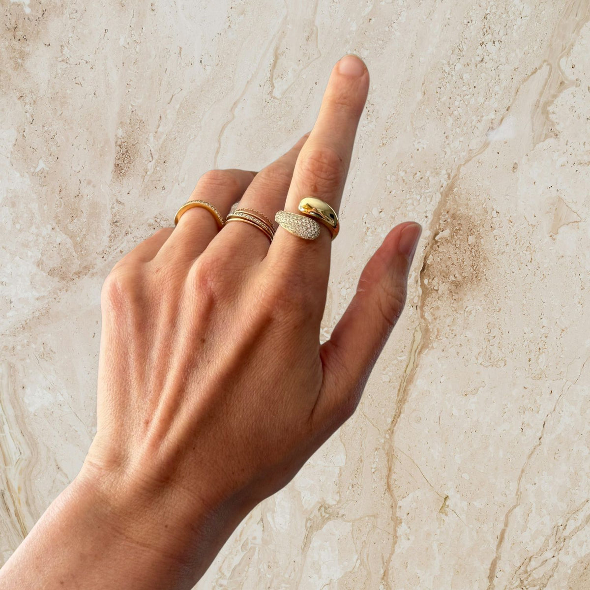 Hand wearing multiple gold rings on a marble background