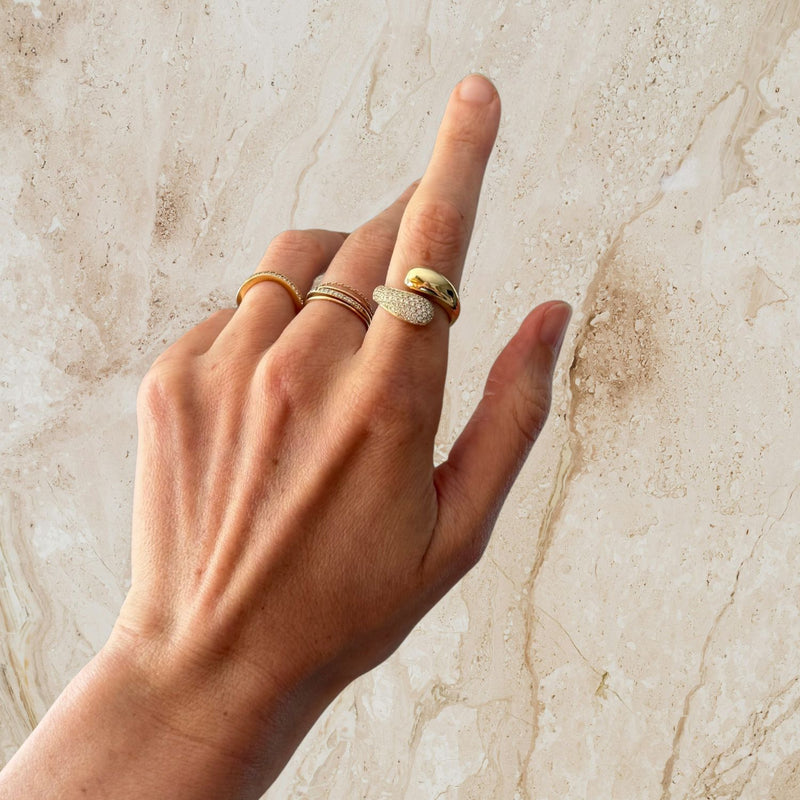Hand wearing multiple gold rings on a marble background